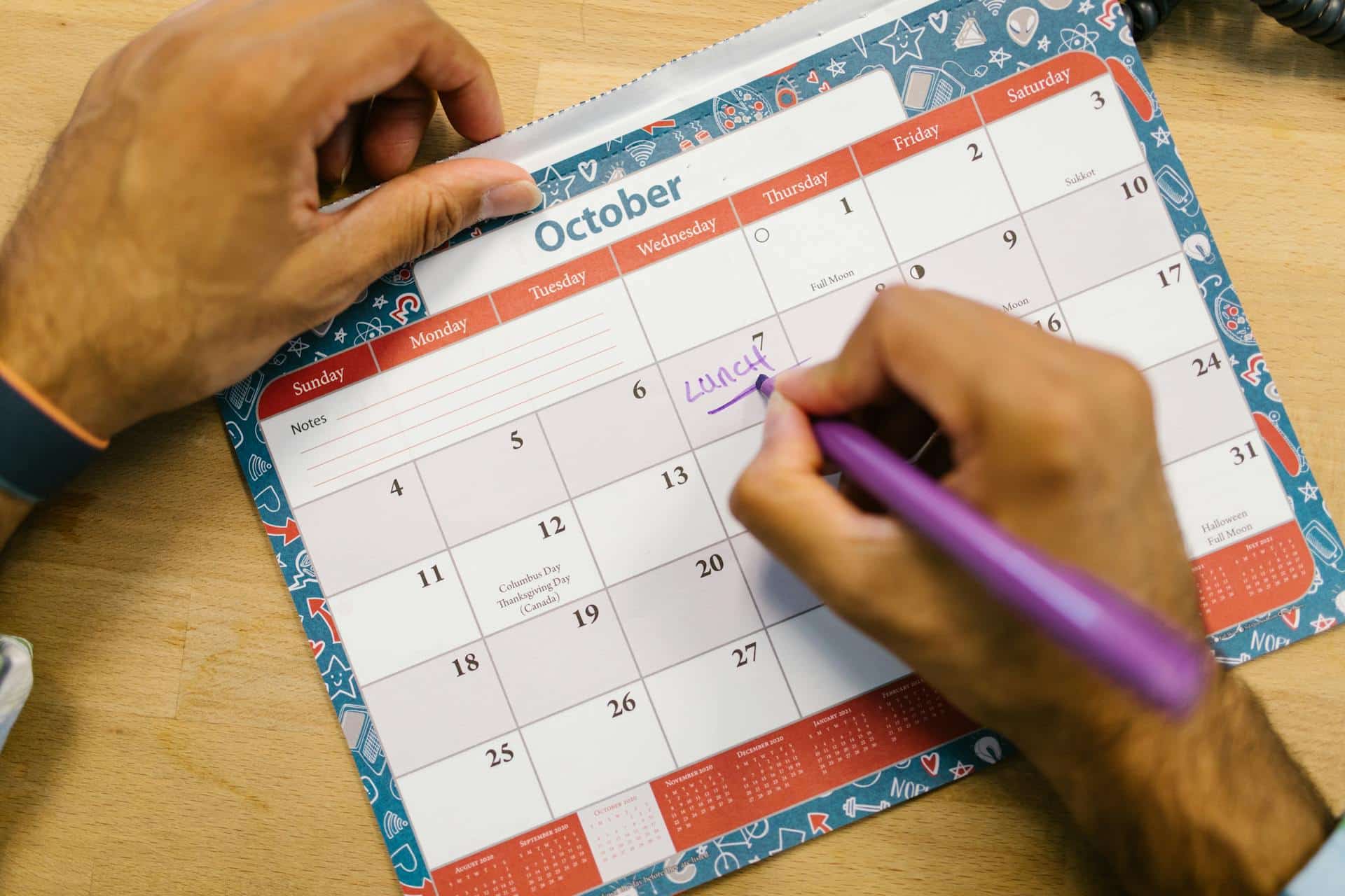Person writing on a calendar with a pink pen
